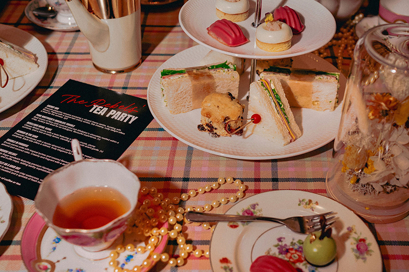 A table set with teacups, plates, and hightea sandwiches