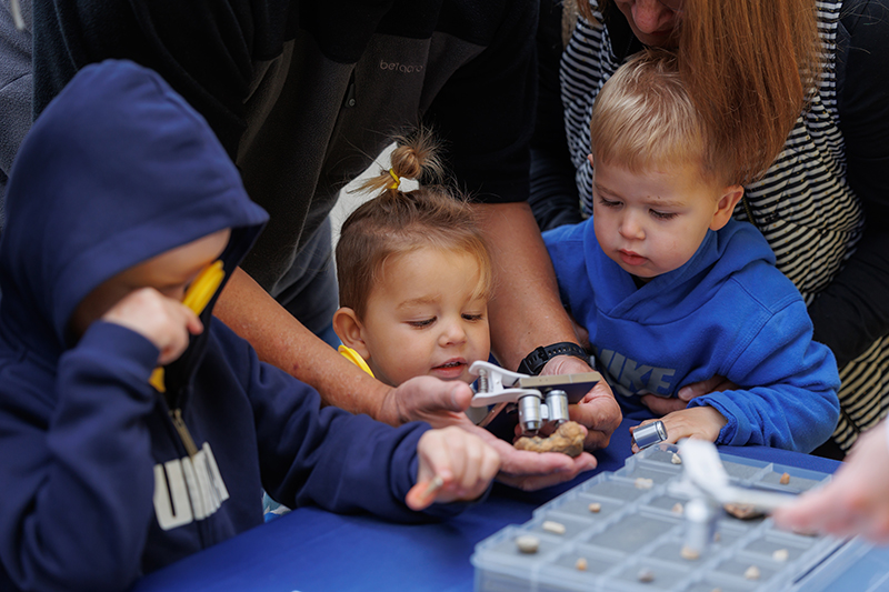 Three children are looking at a small stone through a magnifying glass.