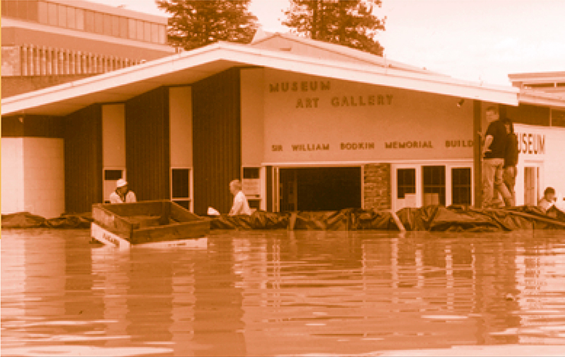 A sepia toned photo of people retrieving items from a flooded museum. The water outside the building is waist high.