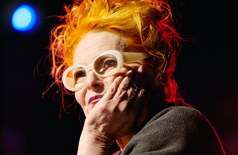 A close photo of a woman holding her hand to her face. She has bright orange hair and a spotlight is shining on her.