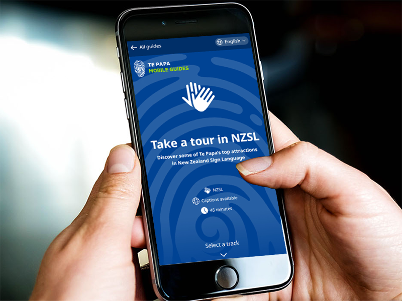 Closeup of hands holding a mobile phone which is displaying the NZSL mobile guide.