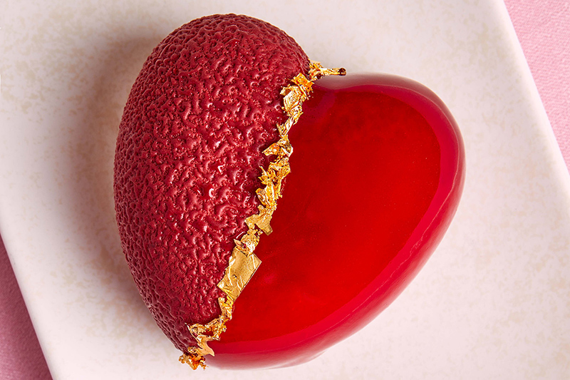 A heart-shaped desert on a plate. The heart has gold leaf down the middle of it and one side is rough and one side is smooth.