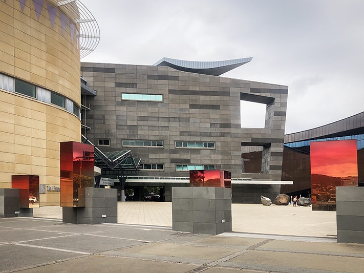 Merging Blocks (2024) by Sabine Marcelis, The Collin Post 4 Plinths Project. Photo by Jane Harris. Te Papa (257445) A photo of the forecourt of Te Papa with four concrete blocks lined up. Each of the blocks has a mirrored-glass rectangle at different positions on each.