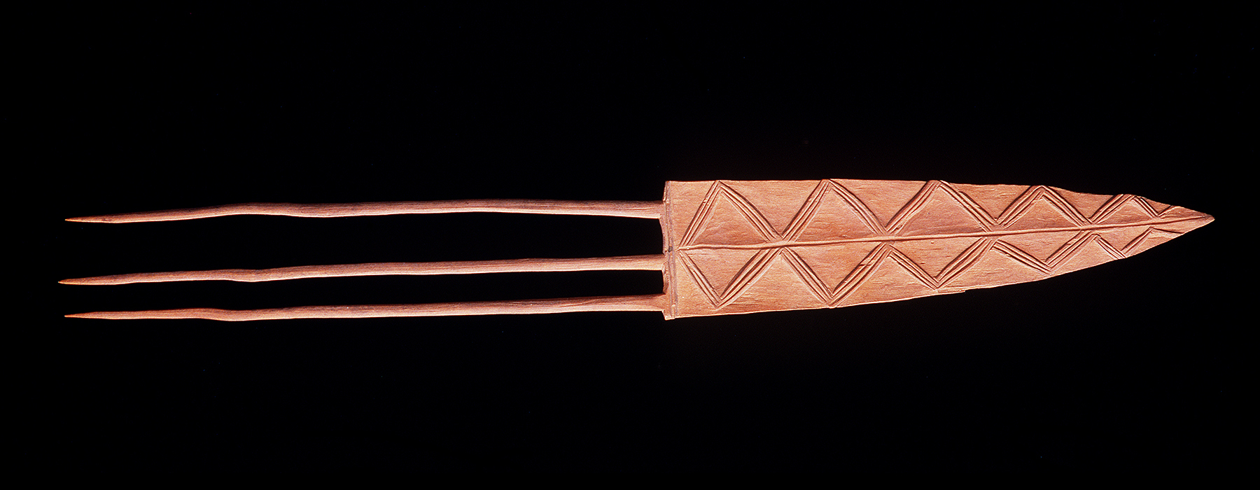 A wooden head comb in the shape of an arrow with three prongs.