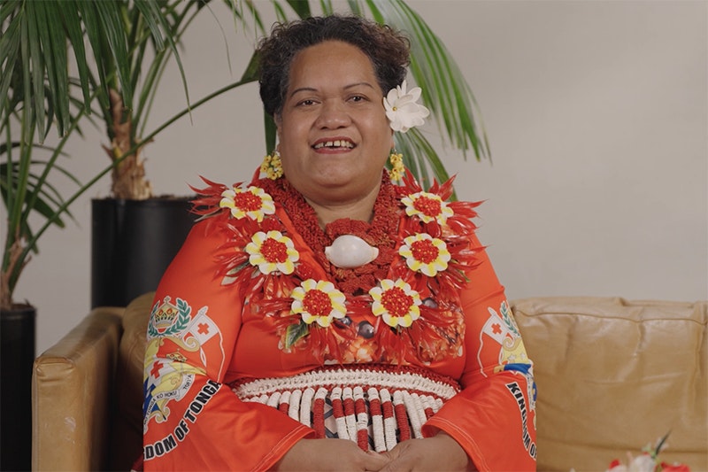 A woman in a bright red dress with a flower wreath around her neck and a single flower behind her ear