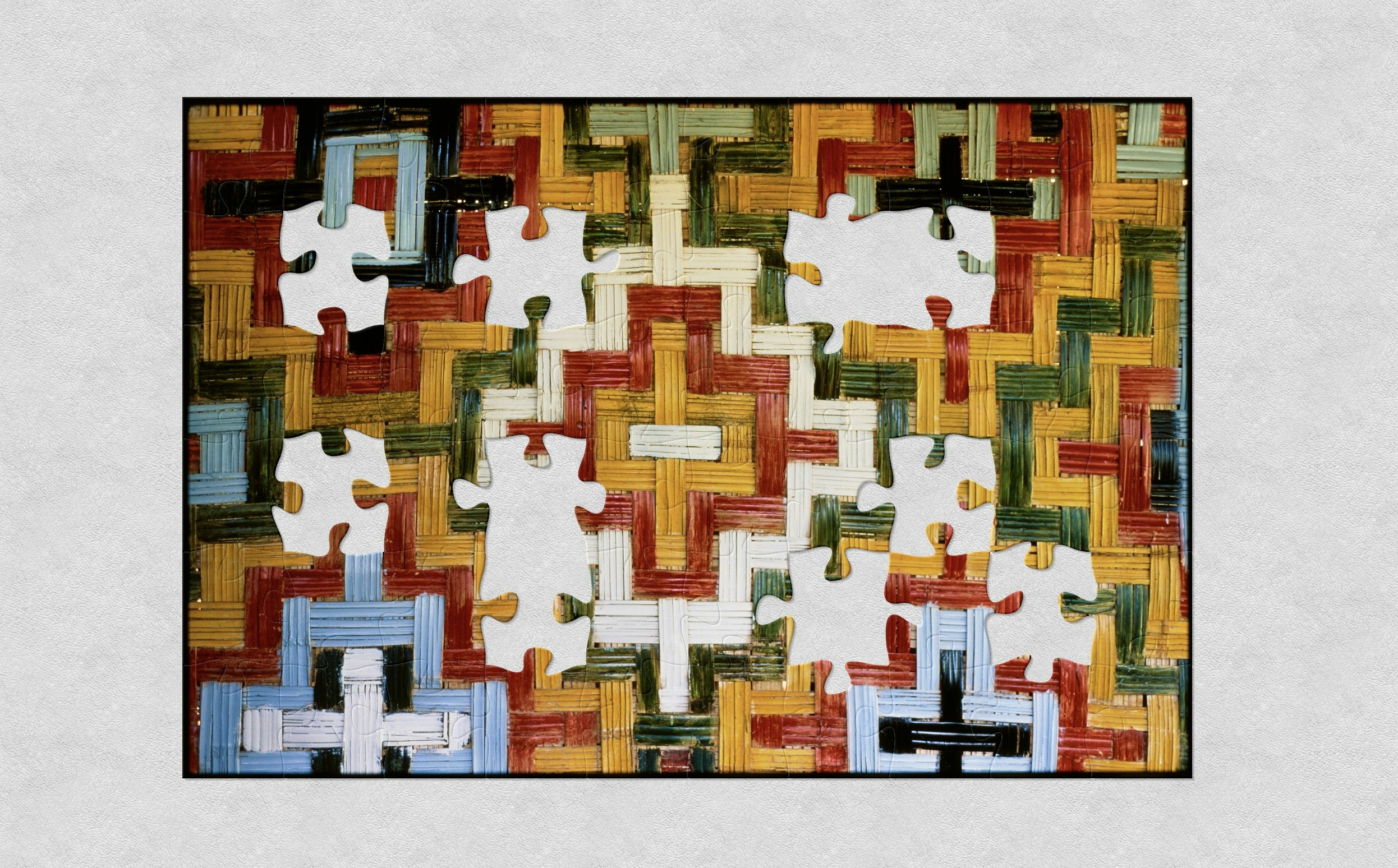 A close photo of a woven wall with the weaving painted in yellow, red, greem, black, light blue, and white, in a step diamond pattern with jigsaw shaped pieces missing.