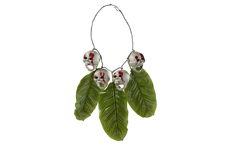 A necklace with four skulls sitting on three large green leaves