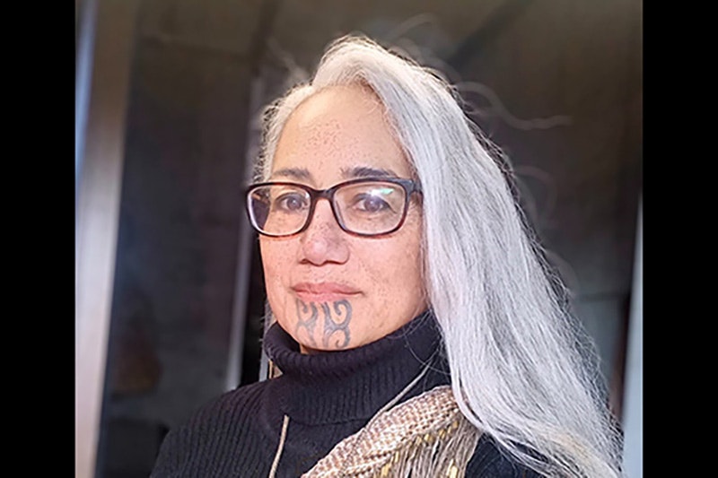 Head and shoulders of a woman with a moko on her chin.