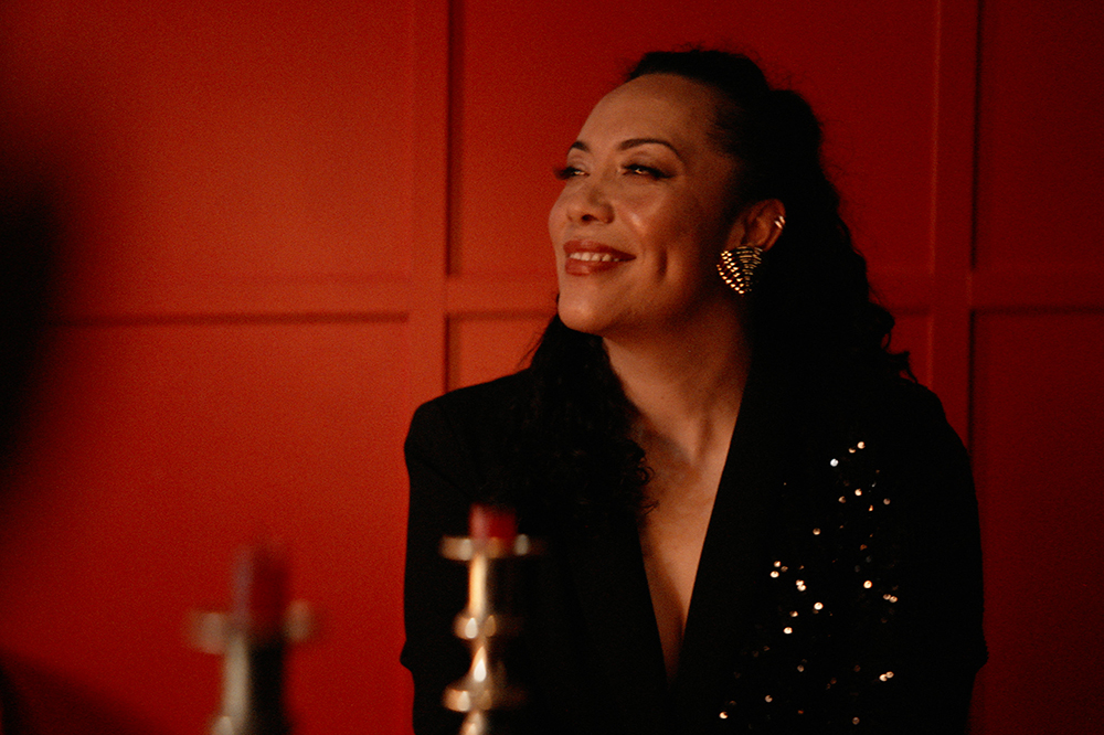 A woman in a sequinned jacket is smiling at something off camera.