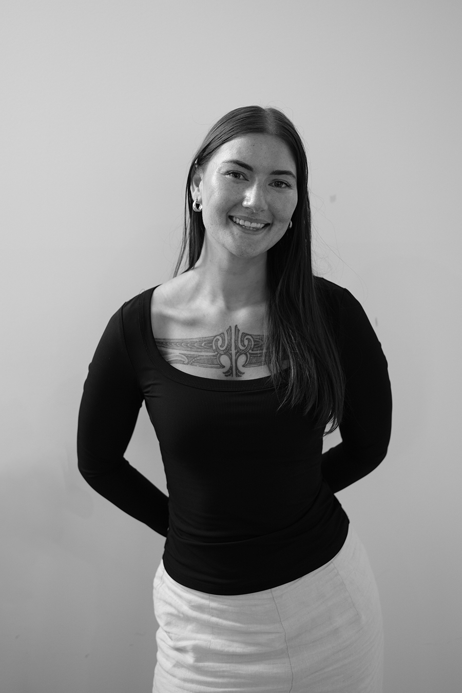 A black and white photo of a woman with long hair and a tā moko tattoo across her chest.