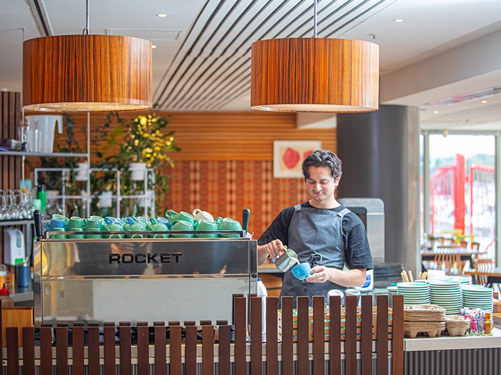 Te Papa Cafe, 2025. Photo by Jeff McEwan. Te Papa (267119) A person is standing at a coffee counter pouring milk into a cup.