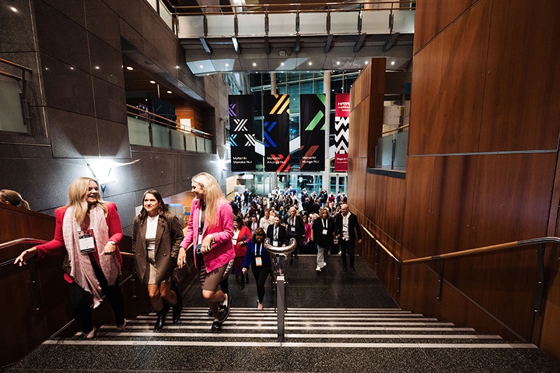 A lot of people walking up the stairs at a museum at night.