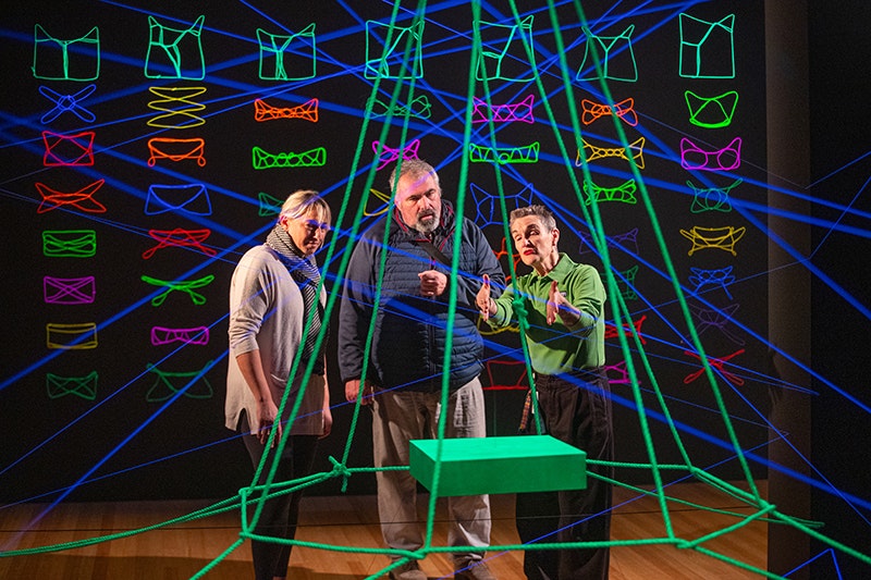 A person in a green shirt is describing an artwork to two other people.