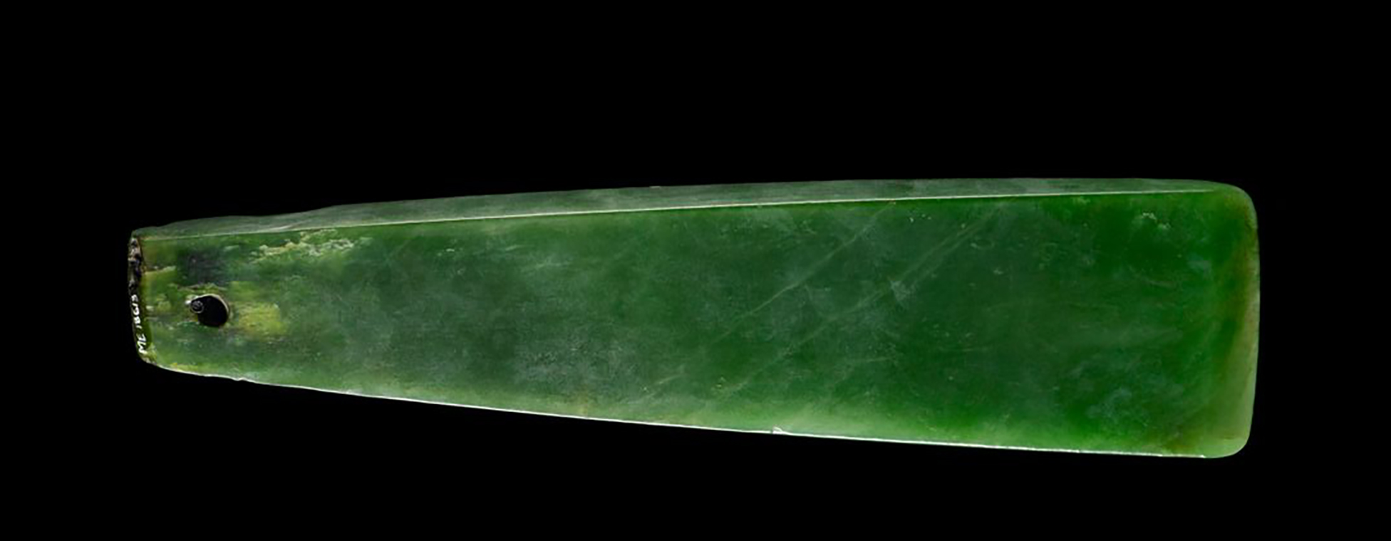 A pounamu greenstone chisel blade on a black background.