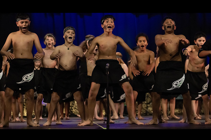 Several young boys are performing kapa haka dance on stage.