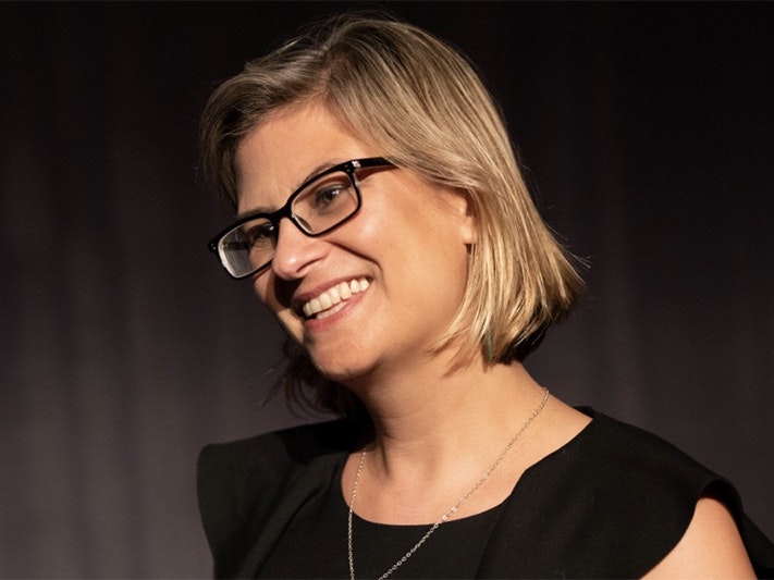 Photo courtesy of Dr Maia Nuku A head and shoulders photo of a woman with blonde hair and glasses smiling at someone off screen.