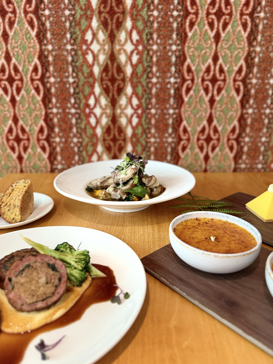 Several plates of food on a table in front of a wall with red, green and white designs.