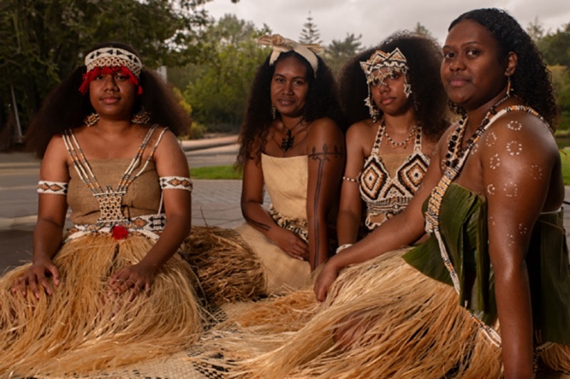 Four women in Solomon Islands dress are sitting on woven mats.