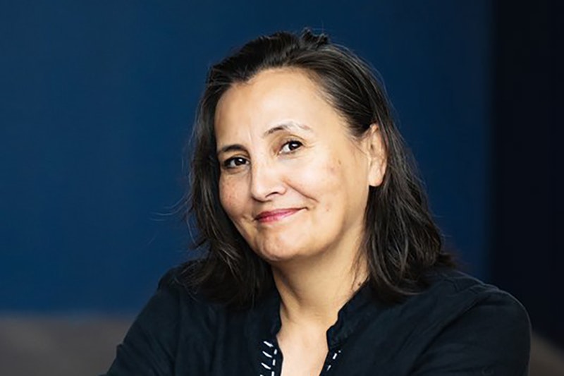 A head and shoulders photo of a woman with dark shoulder-length hair. She is smiling at the camera.