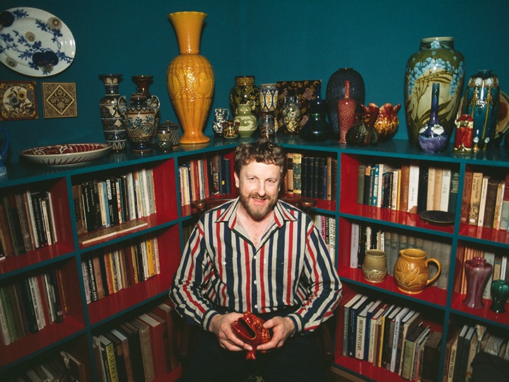 Portrait of Walter Cook, date unknown. Courtesy of Walter Cook A man in a stripey shirt and beard is smiling and holding a pot in front of a collection of books and pots.