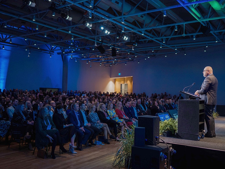 Meetings, Trade Show 2023. Photo by Smoke Photography. Te Papa (274173) A large auditorium with a man in a suit standing at a podium talking to a large seated audience.