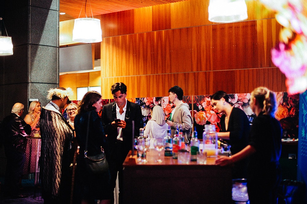 A lot of people standing in a space where there are two people serving drinks.