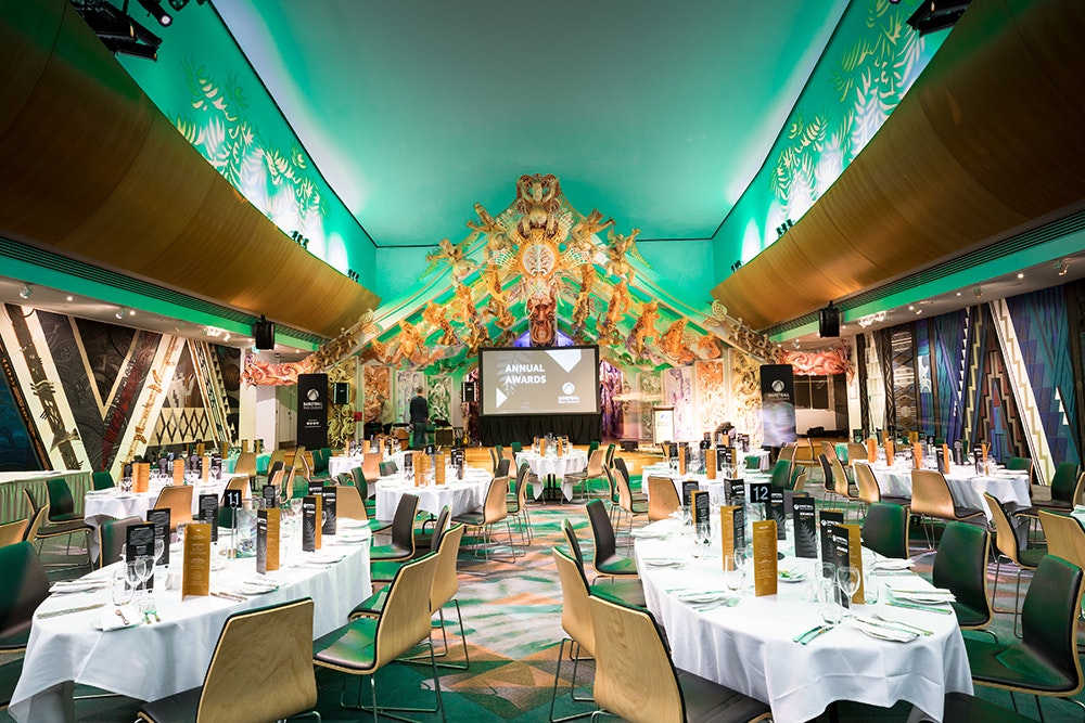 Several tables set for dinner in the marae at Te Papa which has been lit with green lighting.