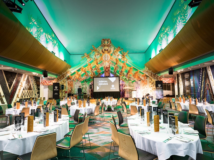 Dinner in Rongomaraeroa, photo by Abbie Dorrington 2019. Te Papa (138437) Several tables set for dinner in the marae at Te Papa which has been lit with green lighting.