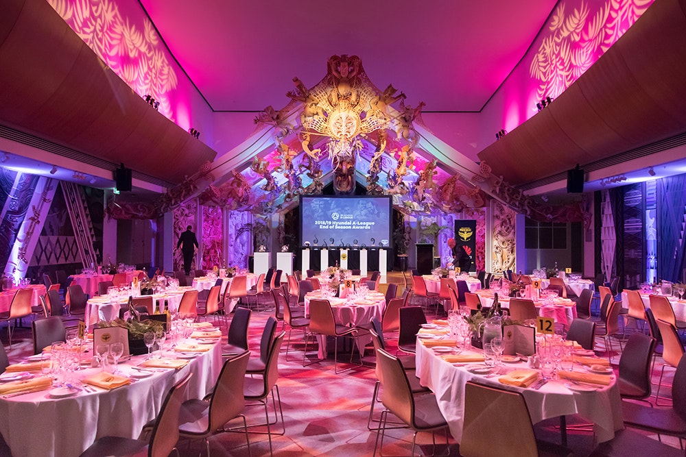 The marae space in Te Papa with pink and purple coloured lighting and tables set up for dinner.