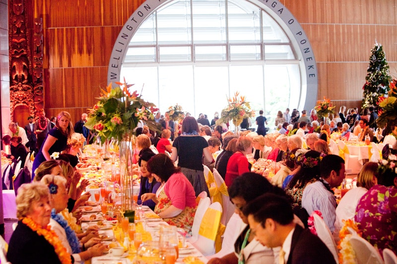 A large gathering is seated at tables set for a wedding.