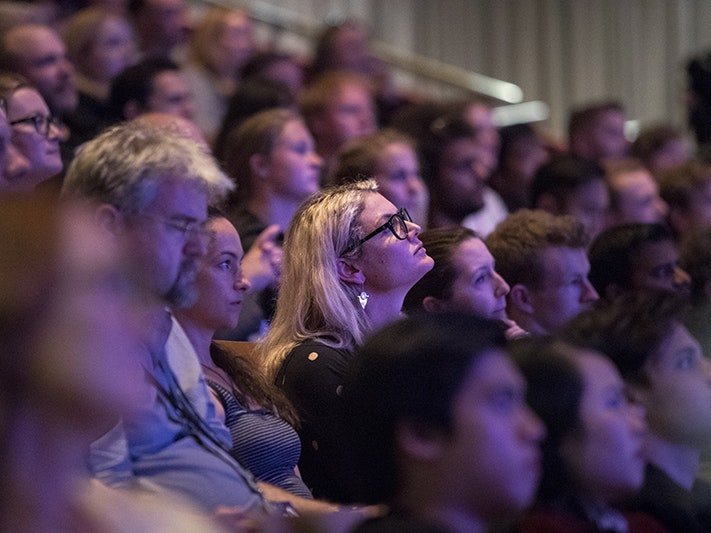 Te Papa Talks: Virtual Realities weekend. Photo by Michael O'Neill. Te Papa Audience members sit closely packed in tiered seating, watching a speaker off camera under low auditorium lighting.