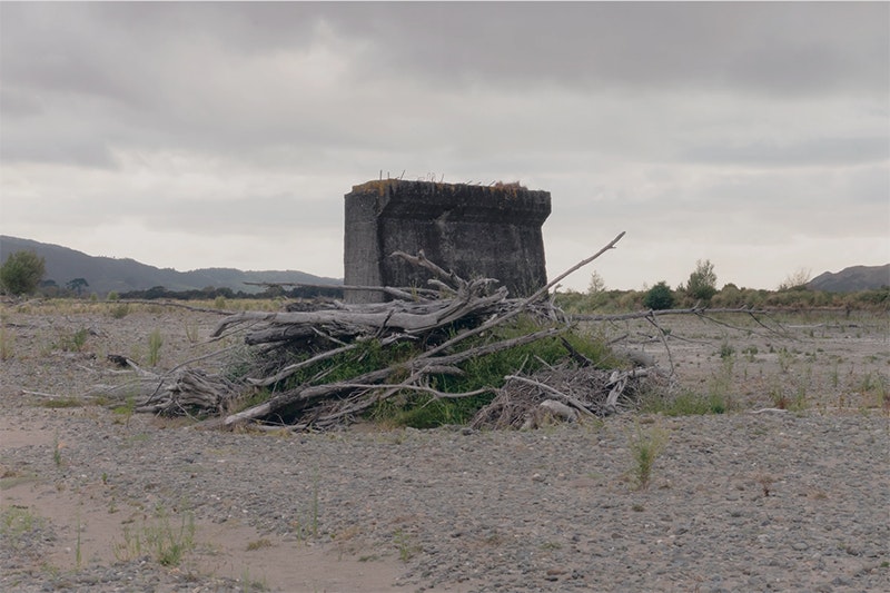 Part of a bridge pier is surrounded by earth and trees.