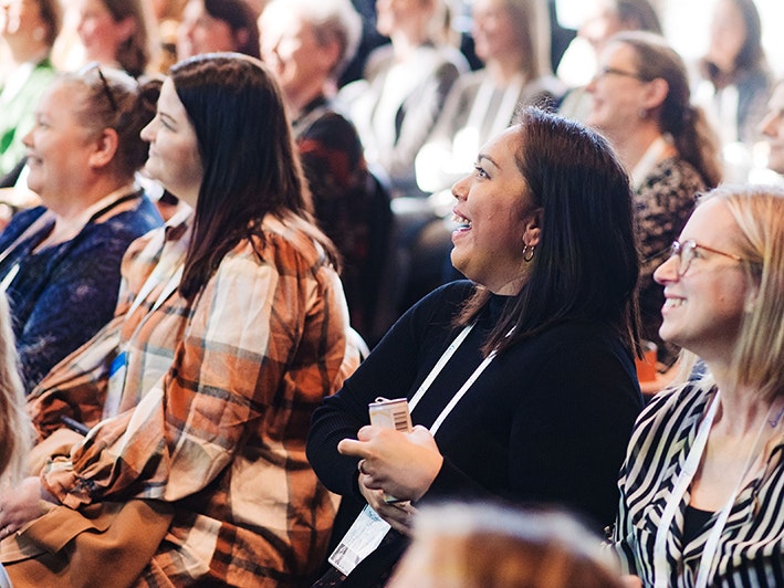 Meetings Tradeshow 2023, Photo by Smoke Photography. People in rows of chairs all laughing at something off camera.