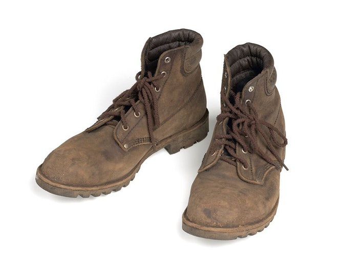 Hec Faulkner outfit; Boots, Kristin Seth; costume designer. Gift of Majestical Pictures Limited, 2019. Te Papa ( GH018346/4) A pair of worn brown boots on a white surface.
