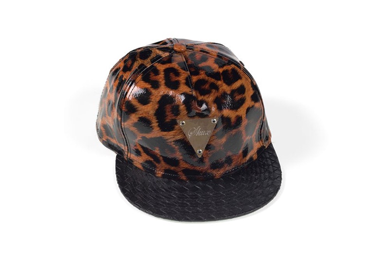 A brown tiger-print cap with a black rim and a label sewn onto it that says "skux".