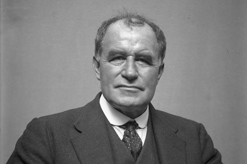 A black and white head and shoulders photo of s man staring at the camera.