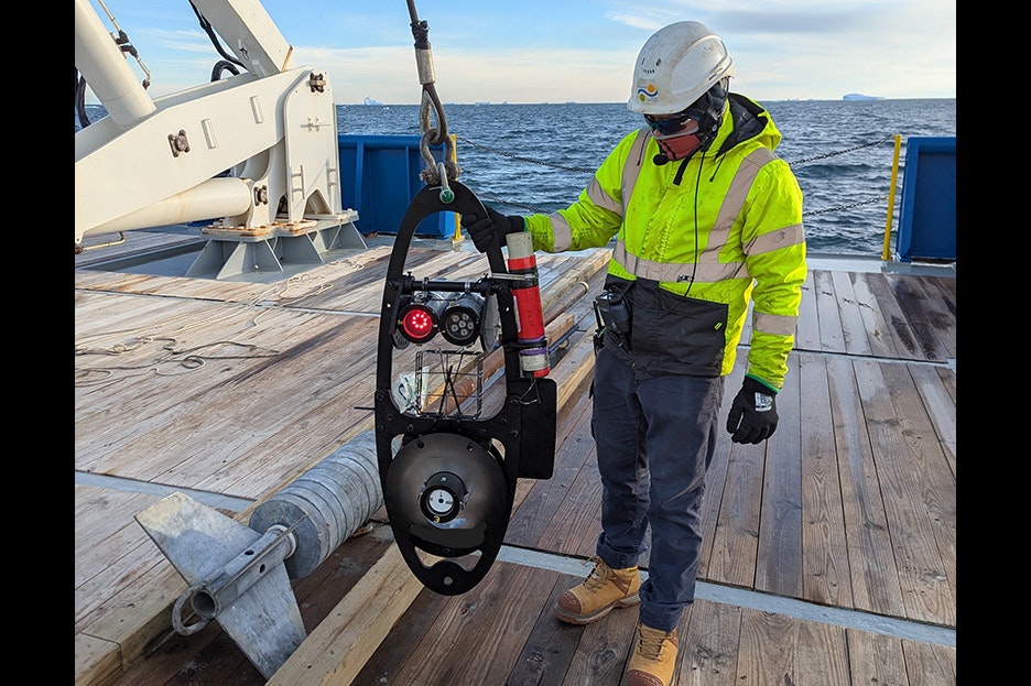 A person in high vis gear is holding piece of scientific equiment on a rope on a boat.